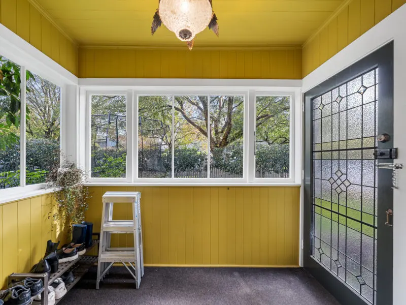 Wooden framed front door with decorative glass panels, set beside timber framed windows in a yellow painted entryway.